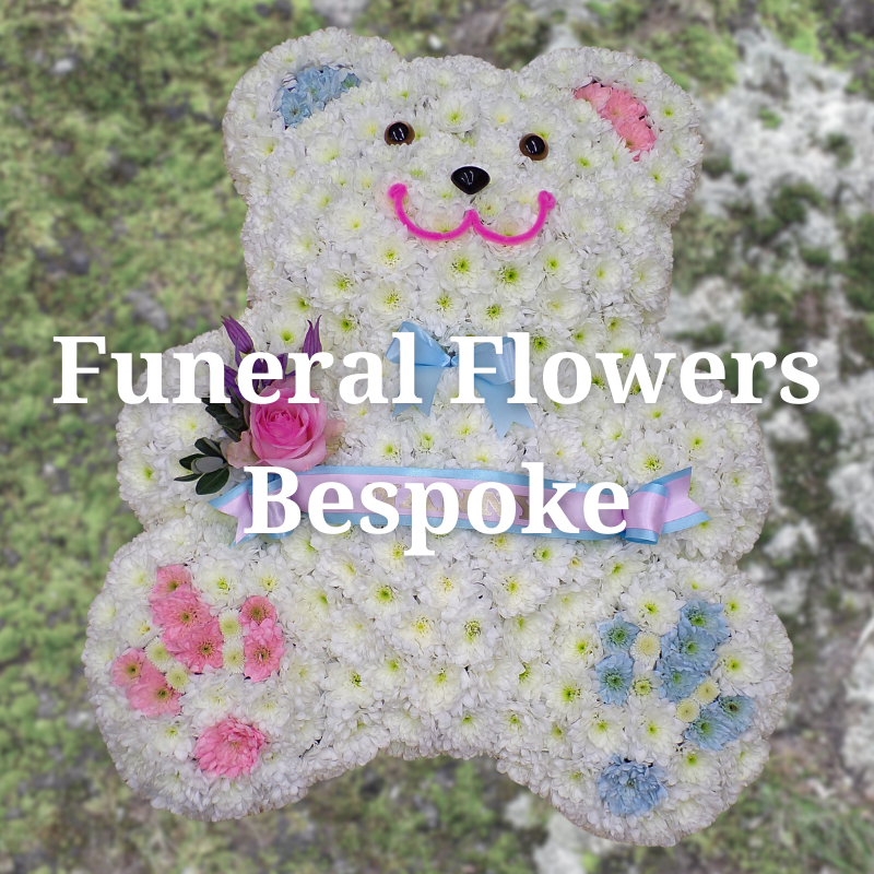 teddy bear-shaped floral tribute made of white flowers with pink and blue accents and a pink rose